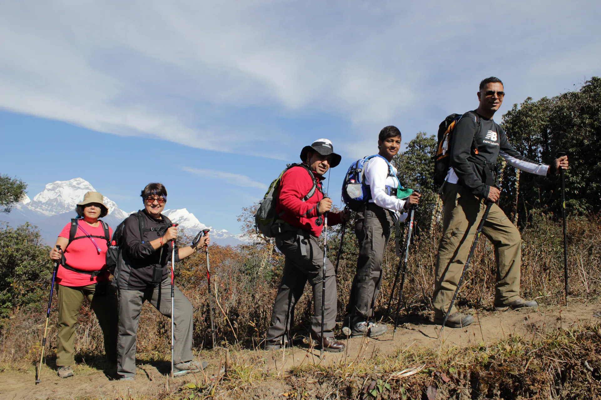 Five trekkers with hiking poles posing on a ridge with Annapurna range behind