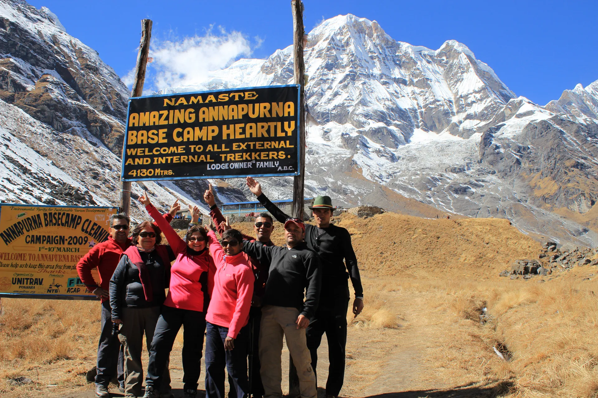 Six trekkers celebrating at the Annapurna Base Camp 4,130m sign with peaks behind