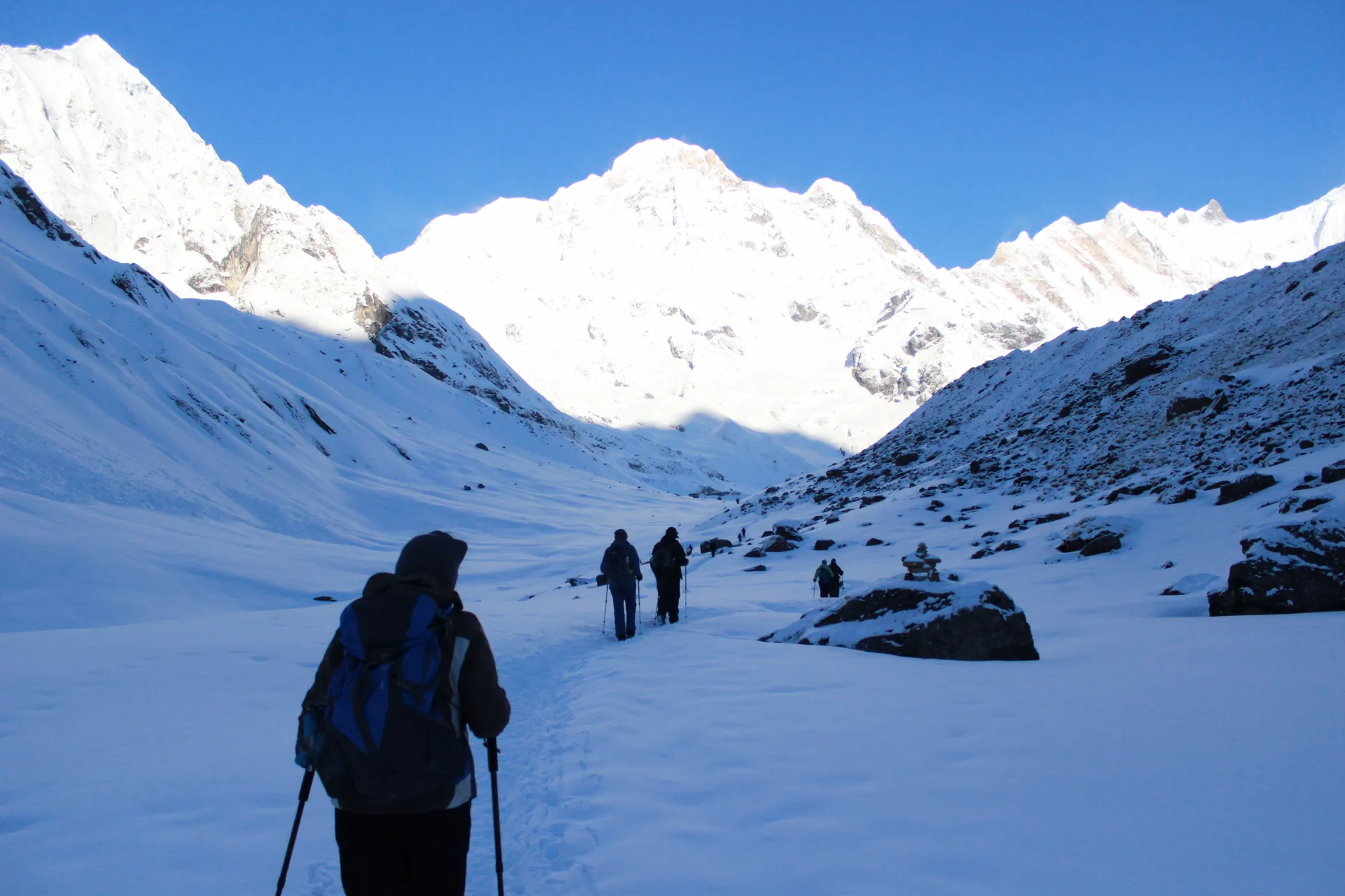 Trekkers walking through deep snow toward Annapurna Base Camp with peaks on both sides