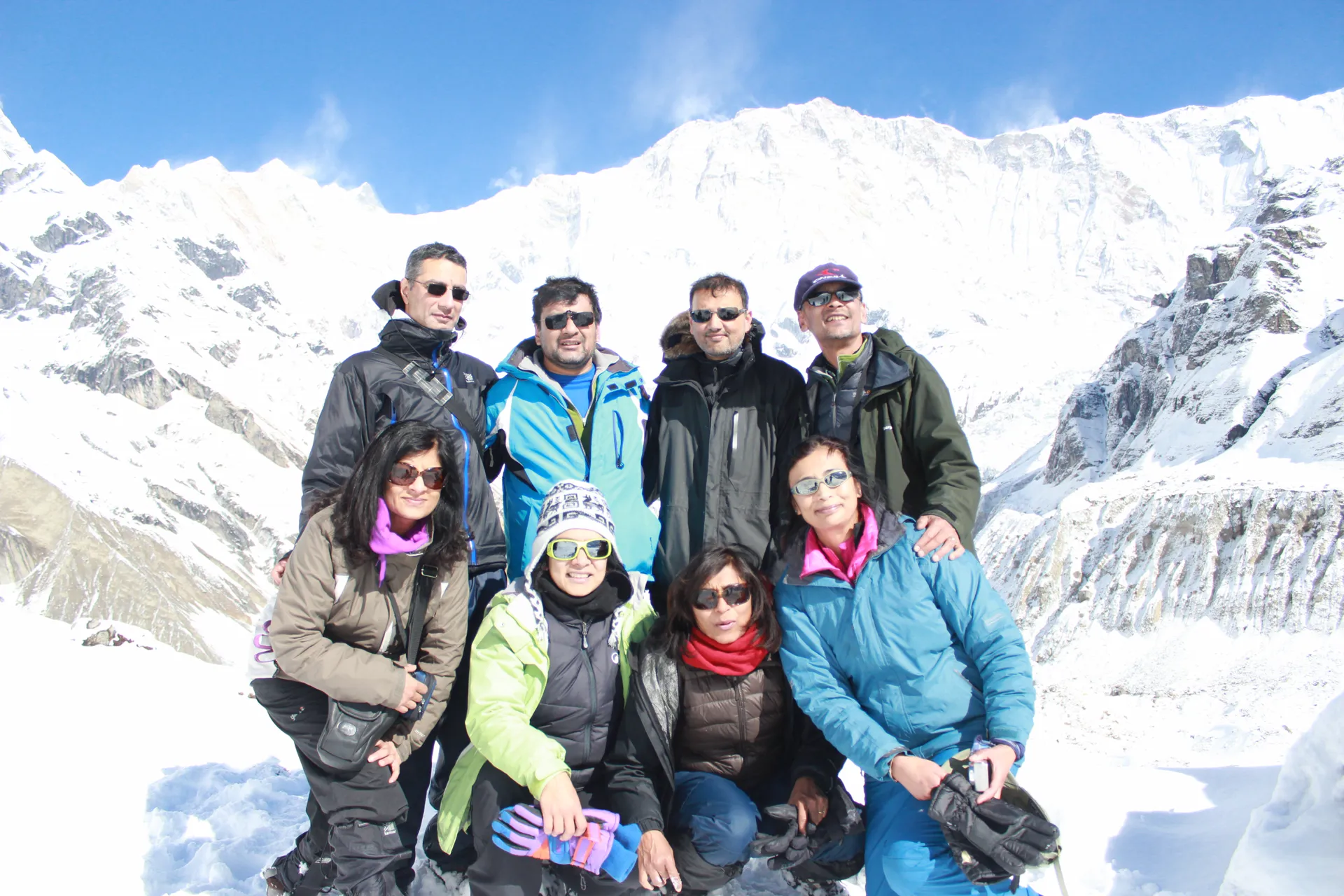 Eight trekkers in winter gear at Annapurna Base Camp with the icy south face behind
