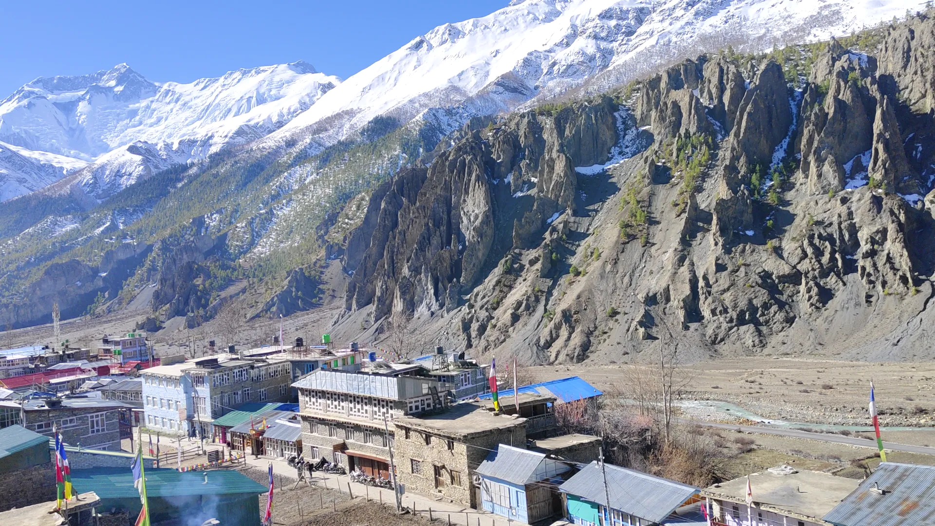 Manang village stone lodges with blue roofs below eroded cliffs and peaks