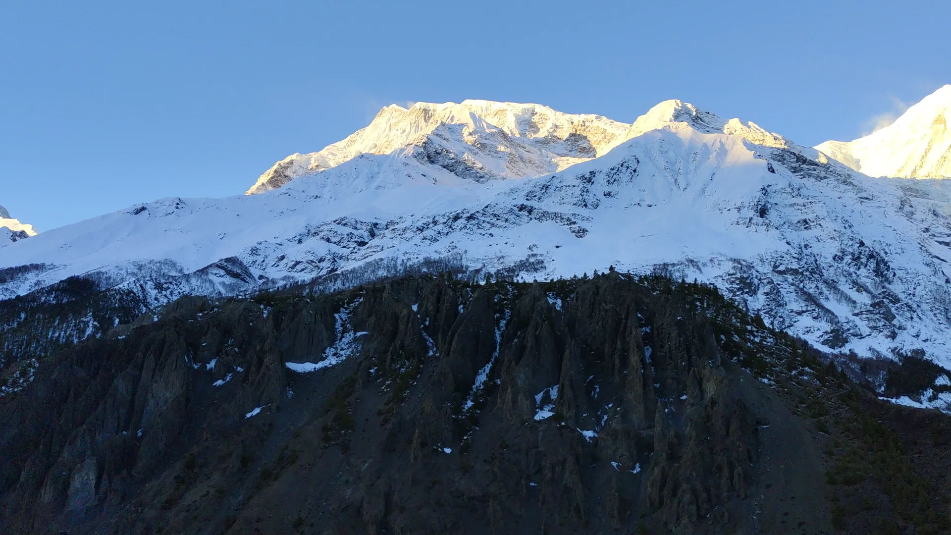 Golden sunrise light hitting snowy Annapurna peaks above a dark ridge