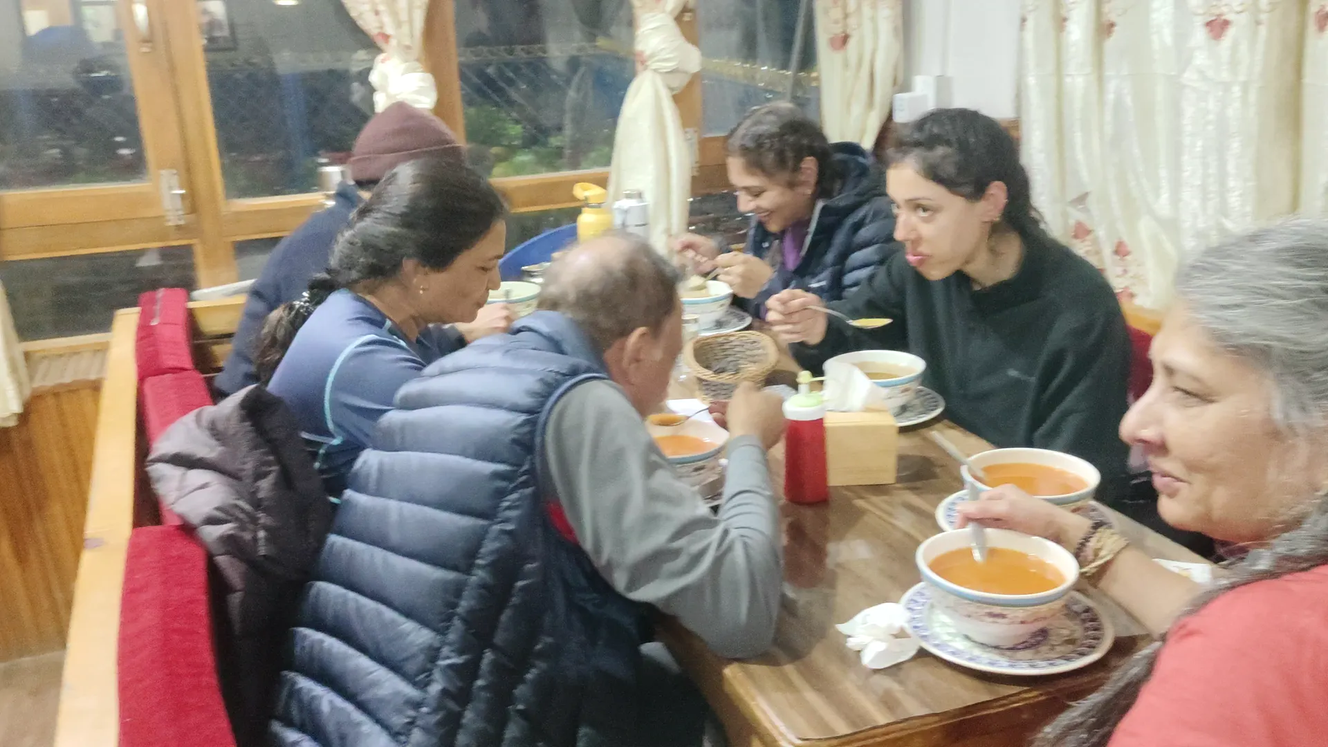 Group of trekkers eating bowls of soup at a teahouse dining table