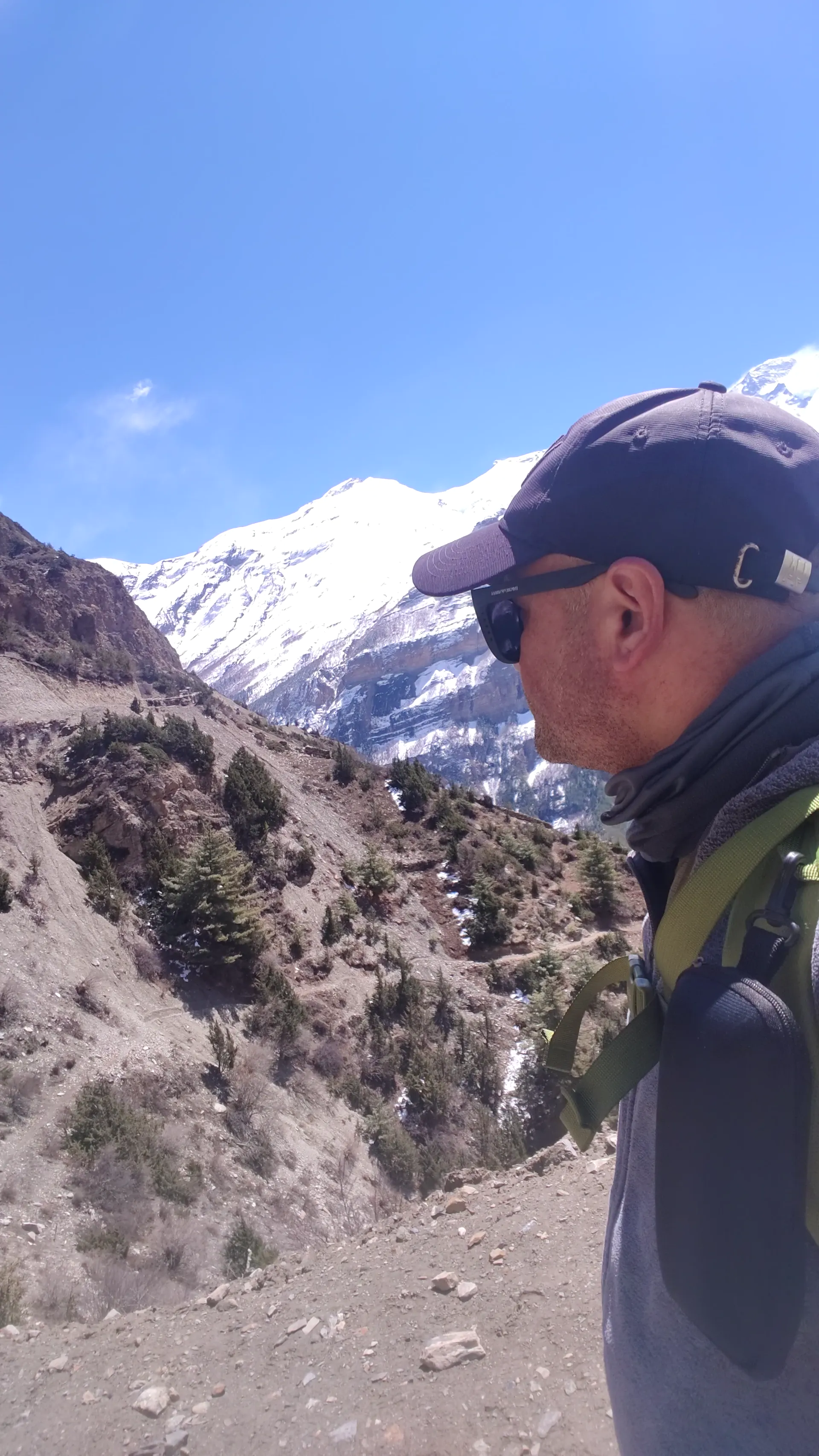 Trekker in cap and sunglasses looking toward snow-covered Annapurna peaks