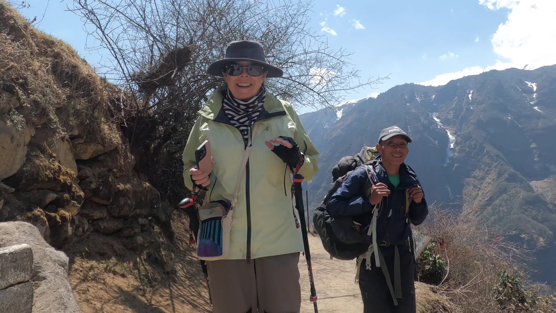 Woman trekker and Sherpa porter with poles on a mountain trail