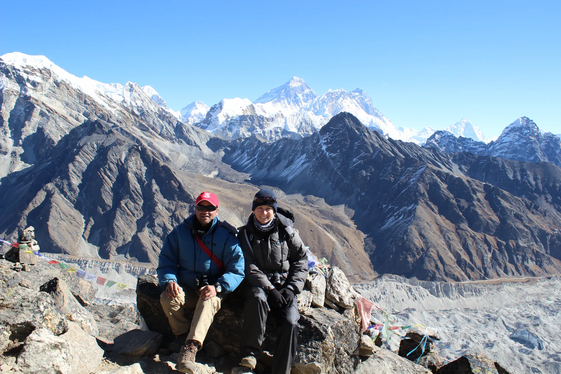 Two trekkers at Gokyo Ri summit with Everest, Lhotse, and Makalu behind