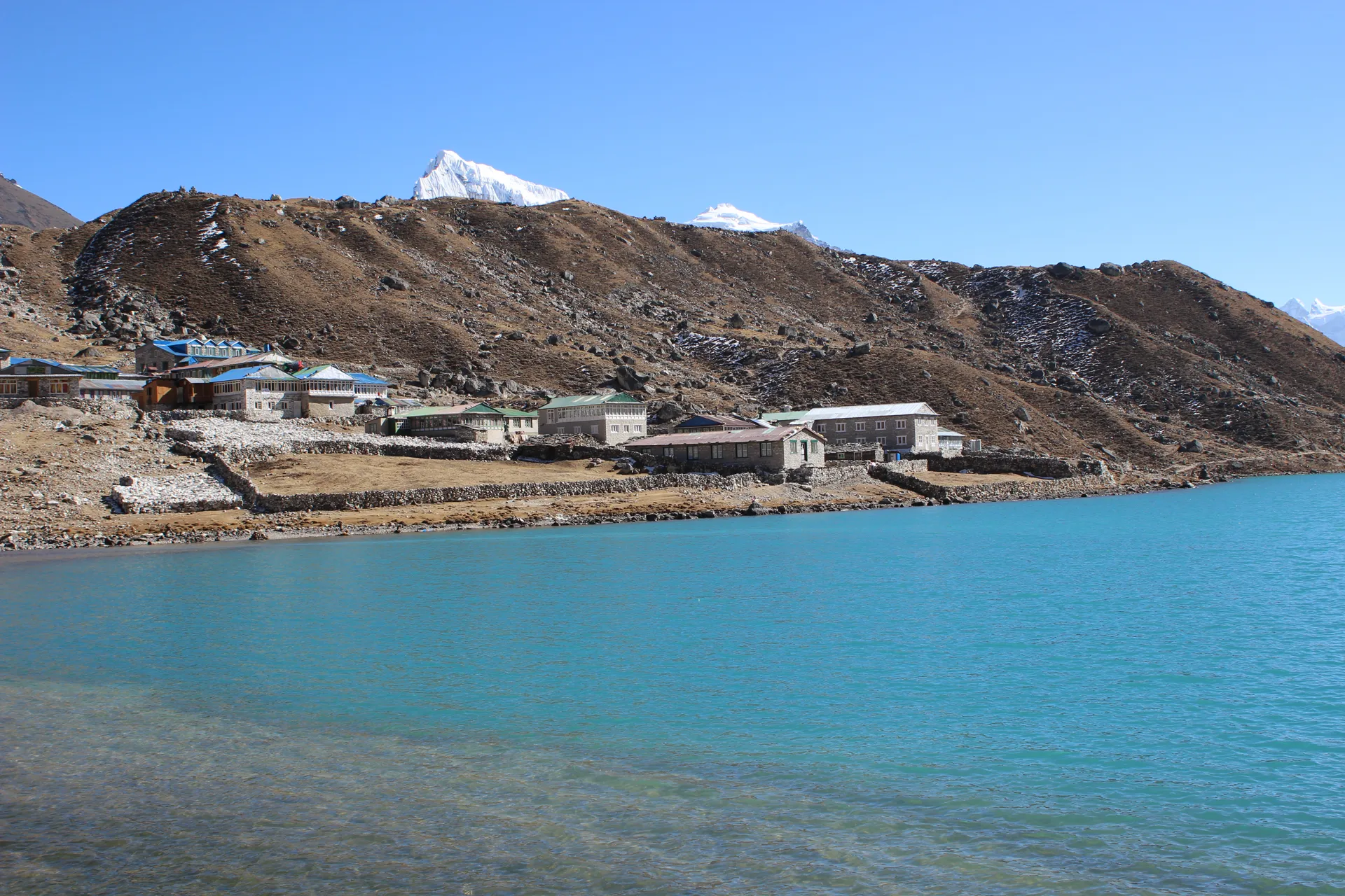 Teahouse lodges along turquoise Gokyo Lake shore with a snow peak behind