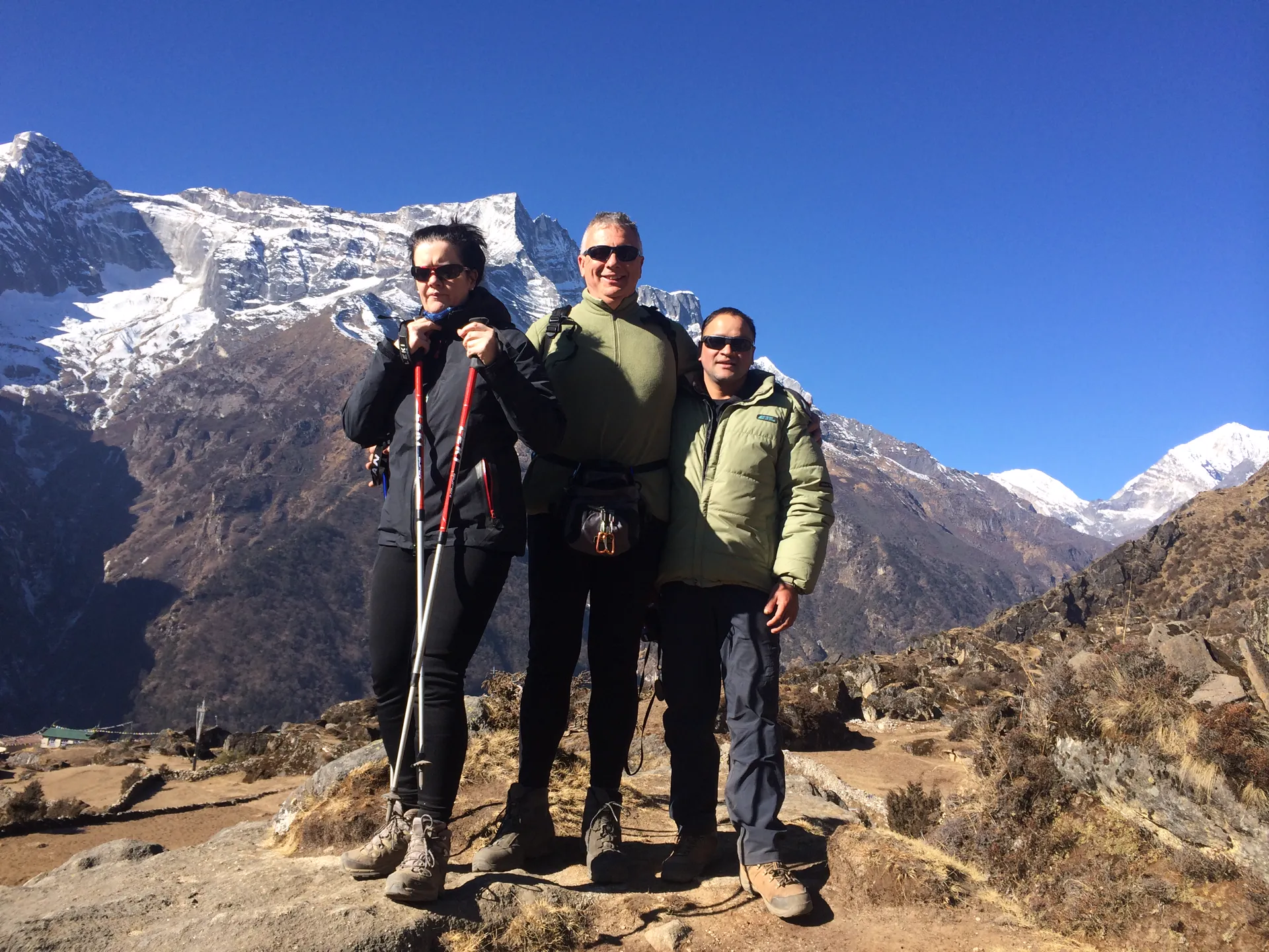 Three trekkers posing on a ridge with snow-covered Himalayan peaks
