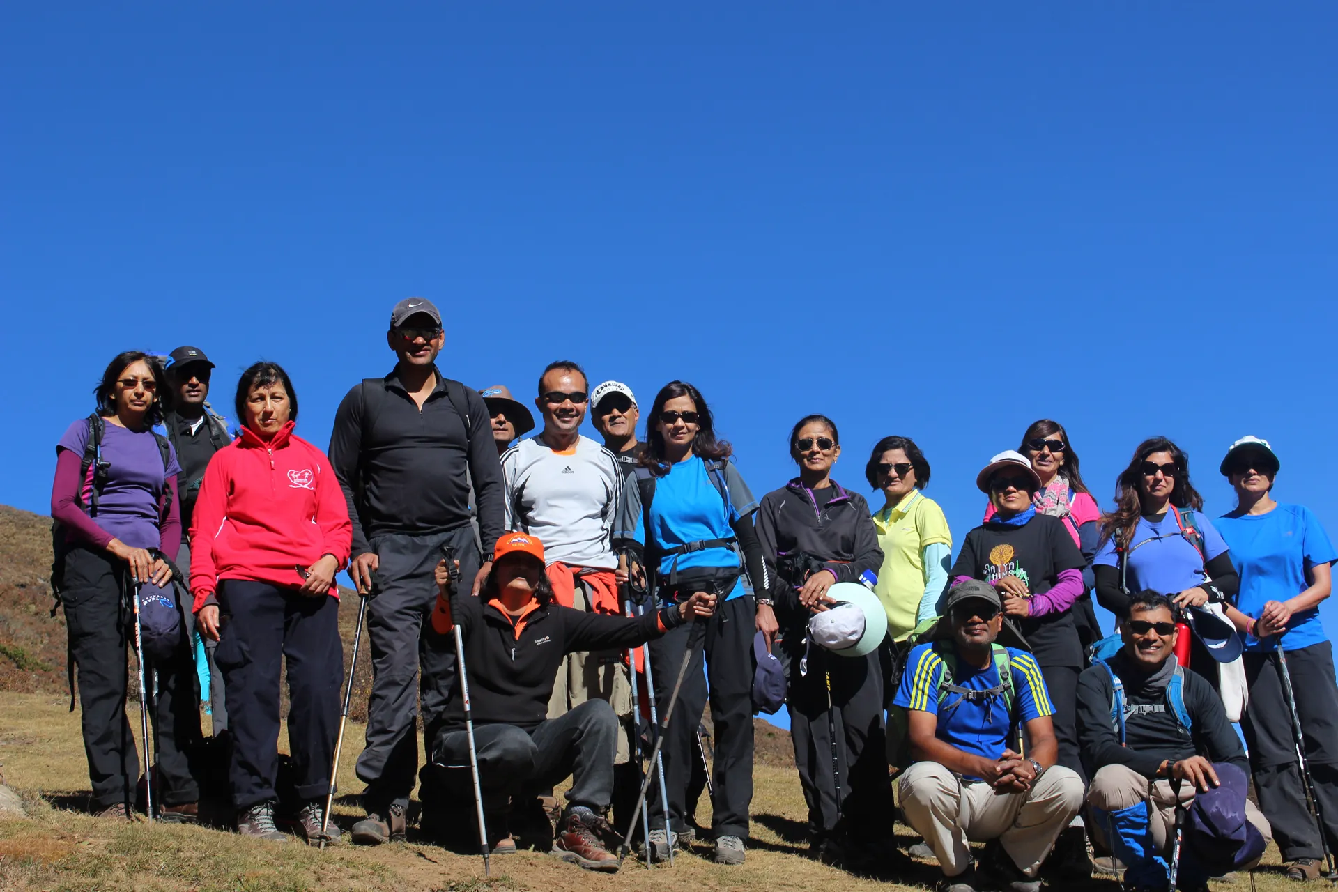 Large trekking group of about twenty people posing on a grassy hillside