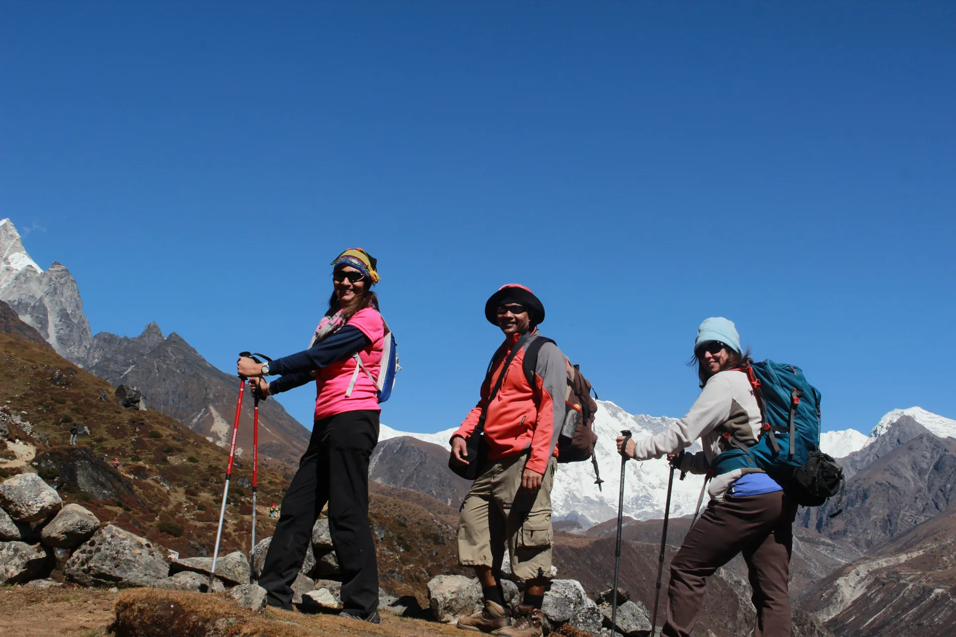 Three trekkers with poles walking along a trail with Cholatse and Taboche