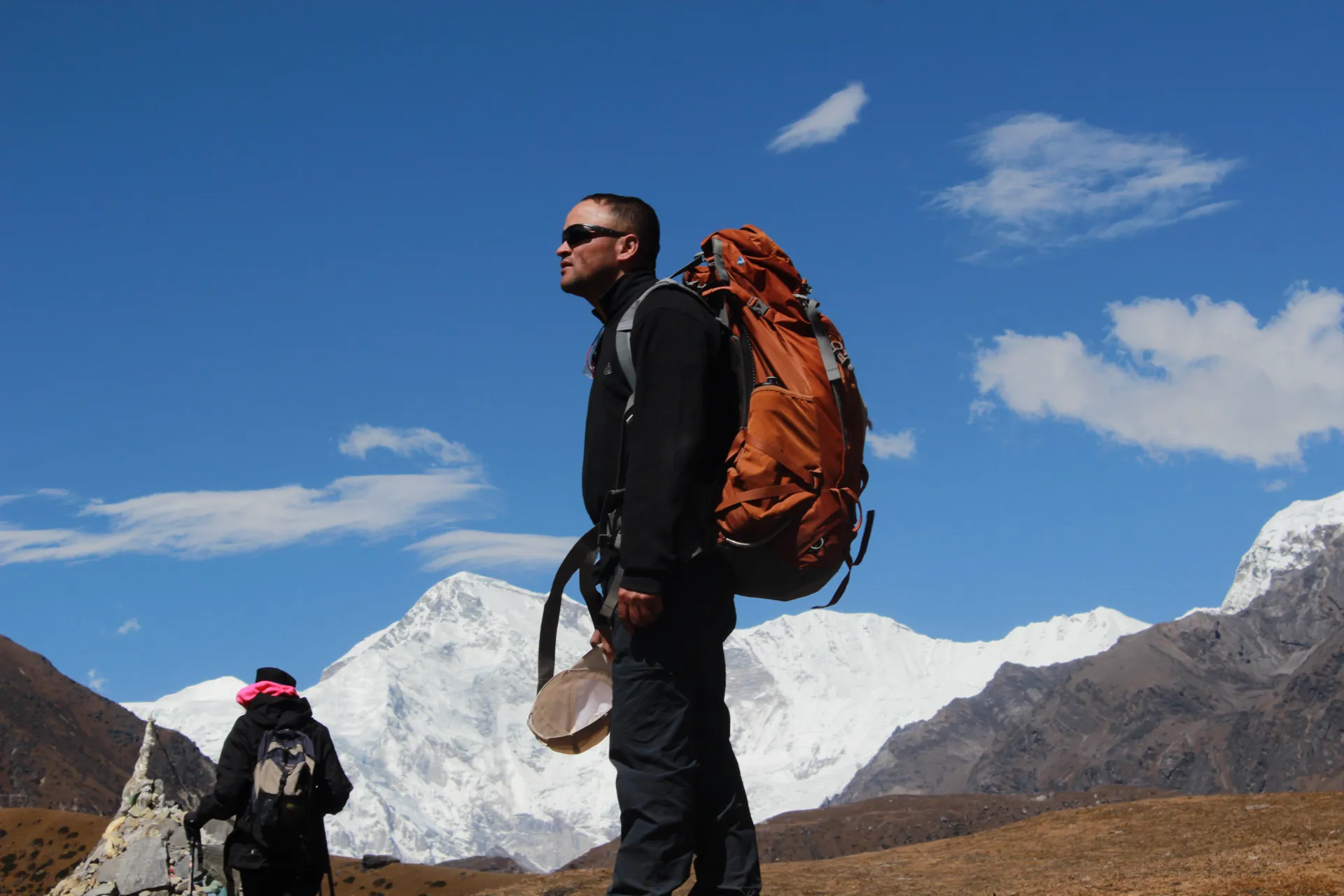 Guide with orange backpack and sunglasses with Cho Oyu and snow peaks