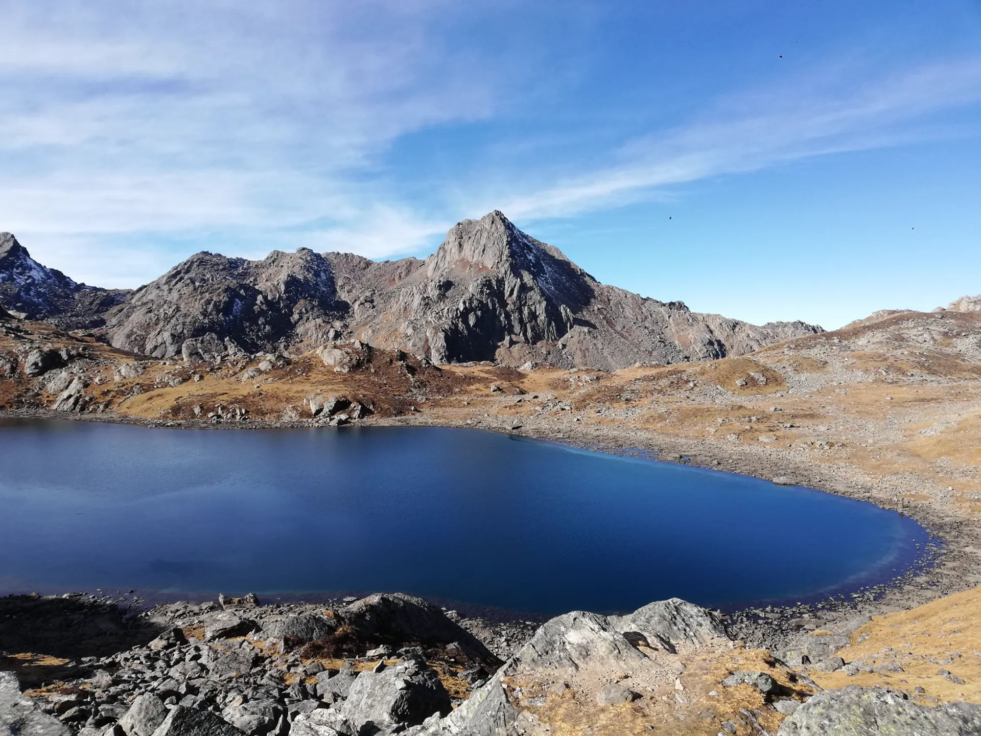 Deep blue Gosaikunda Lake with a pointed rocky peak rising behind the shoreline
