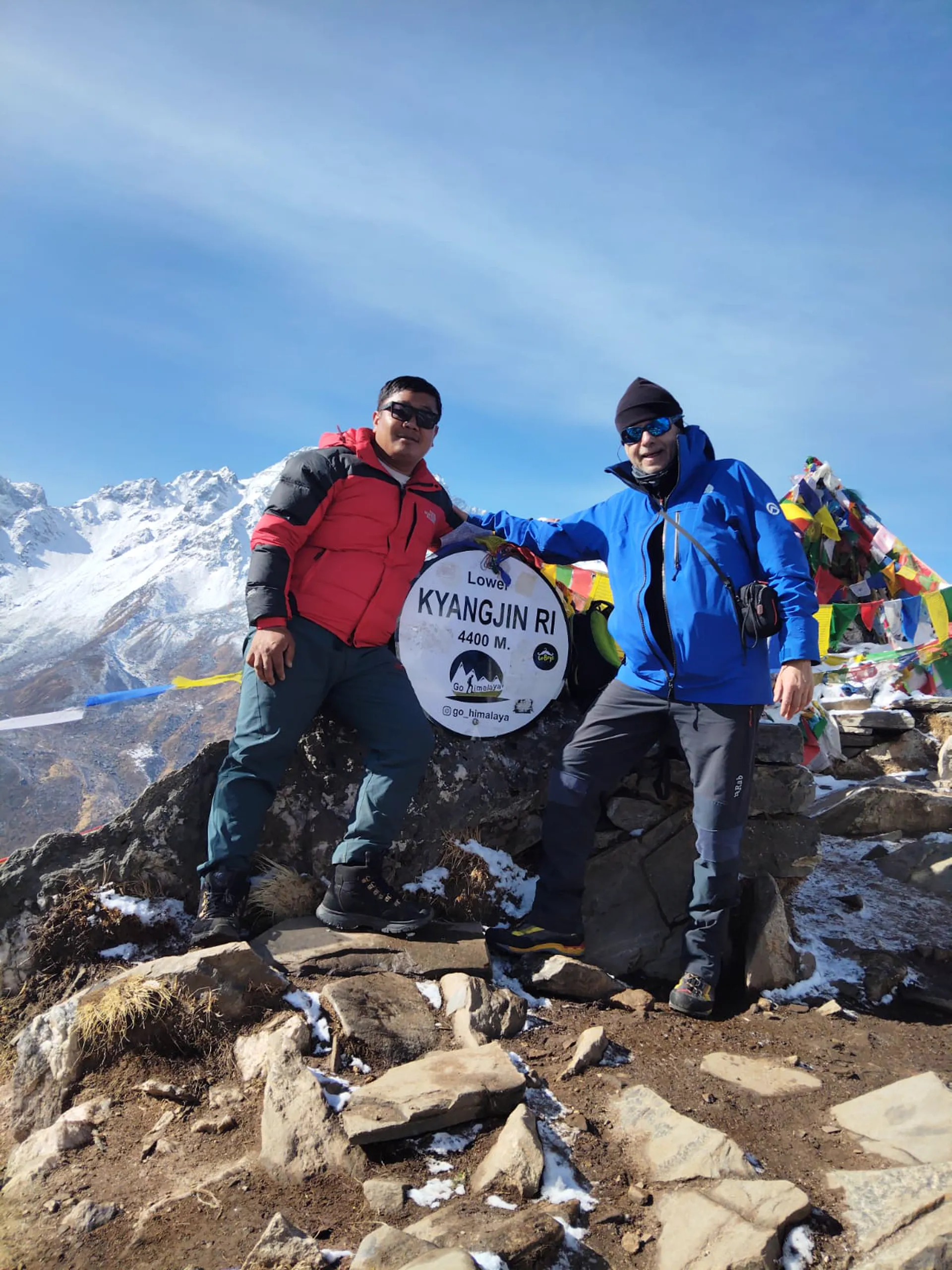 Two trekkers at Kyangjin Ri 4,400m sign with prayer flags and snowy peaks
