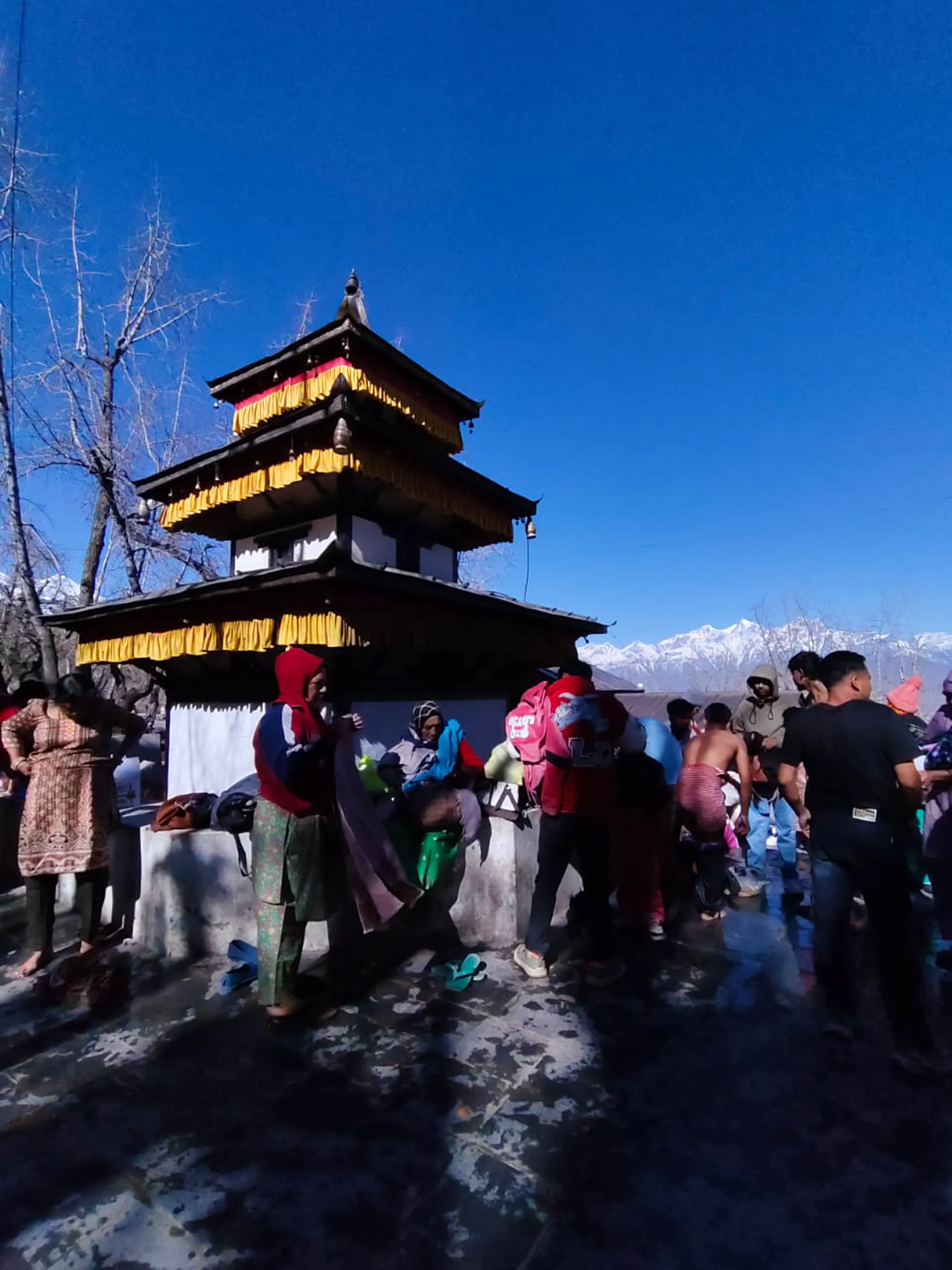 Muktinath Temple three-tiered pagoda with yellow ceremonial cloth and pilgrims gathering for darshan