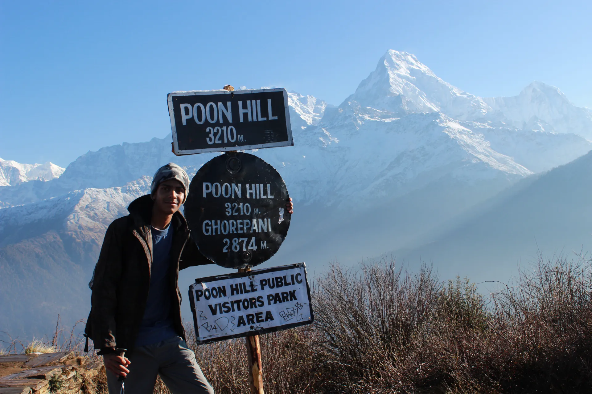 Young man posing beside the Poon Hill 3,210m sign with peaks behind