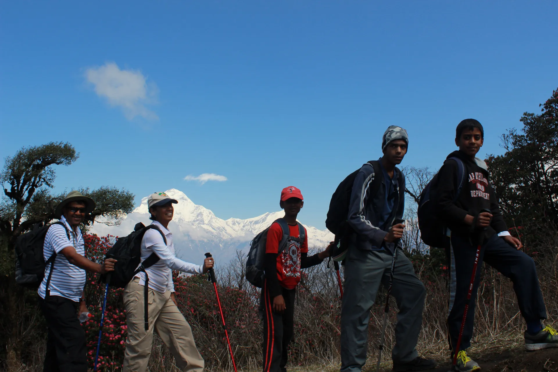 Five trekkers walking along a ridgeline trail with Annapurna range behind