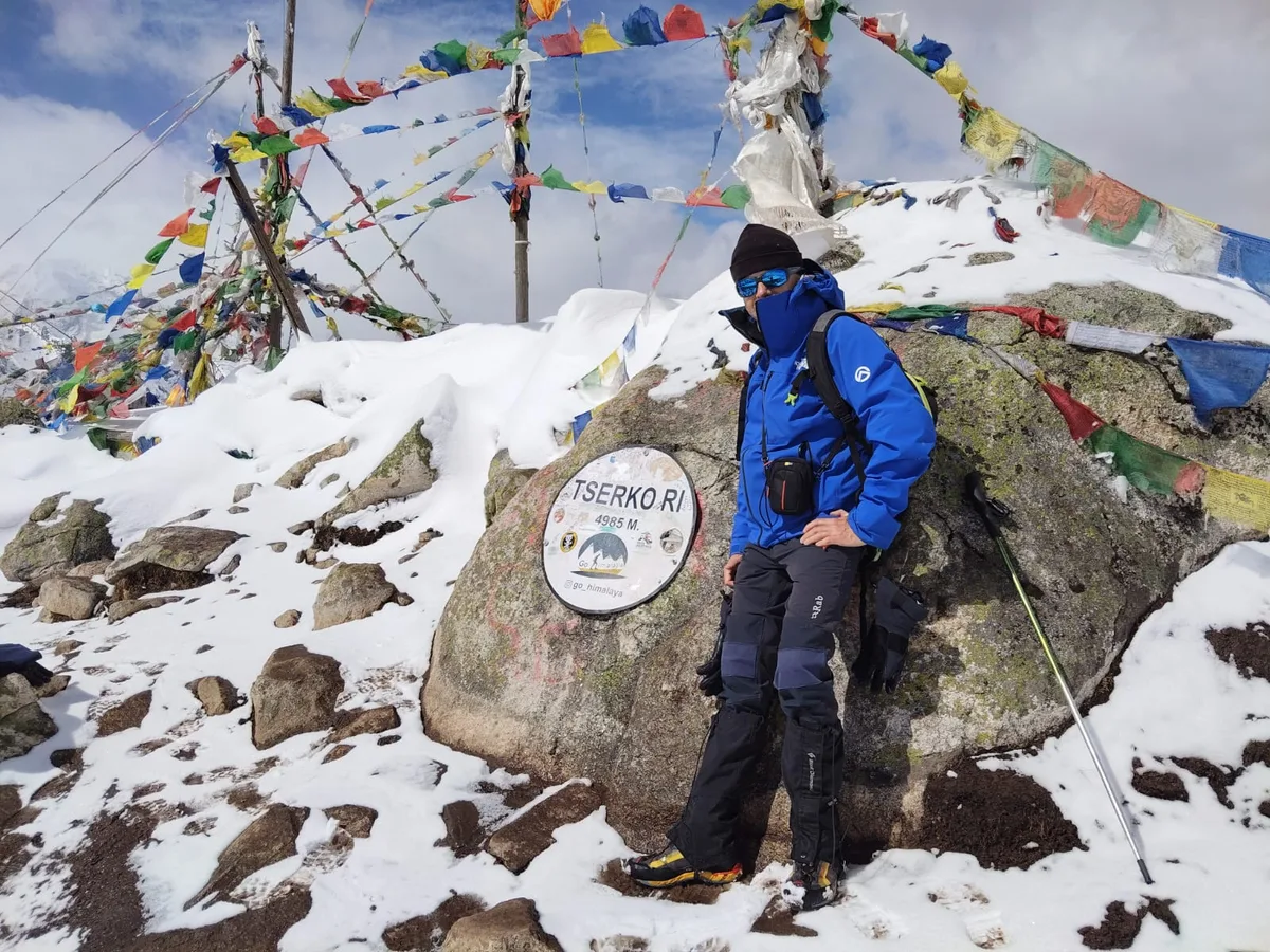 Trekker at Tserko Ri summit marker with prayer flags